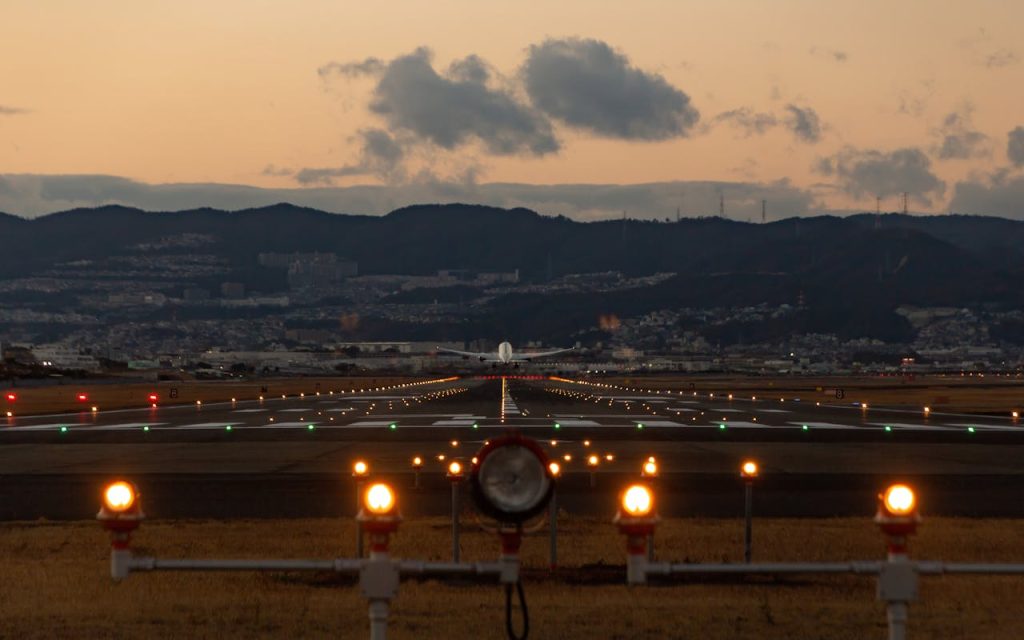 Scenic view of airplane landing on Osaka runway during dusk with city skyline.